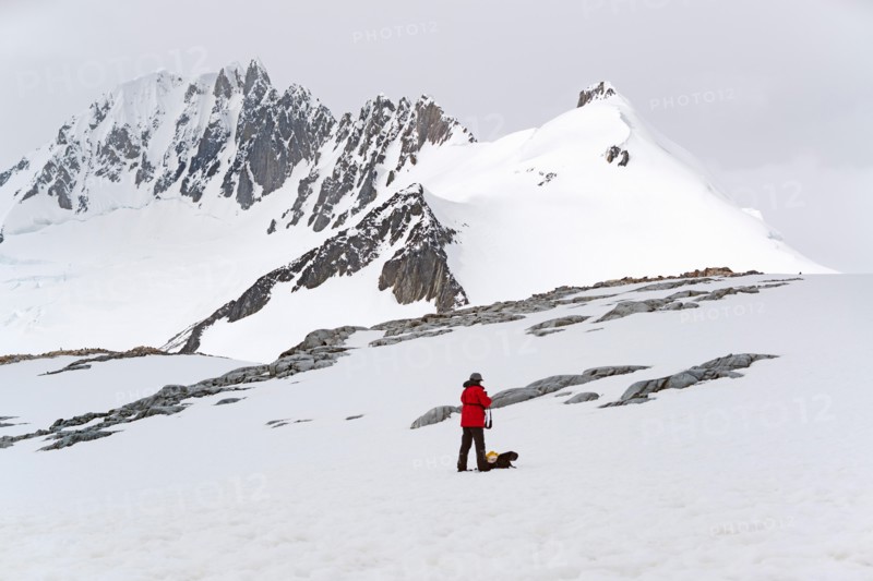 One person standing on the ice in front of a snow-covered mountain.