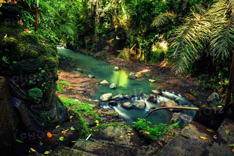 Secret waterfall hidden in tropical jungle with traditional old stone statue on background scenery nature