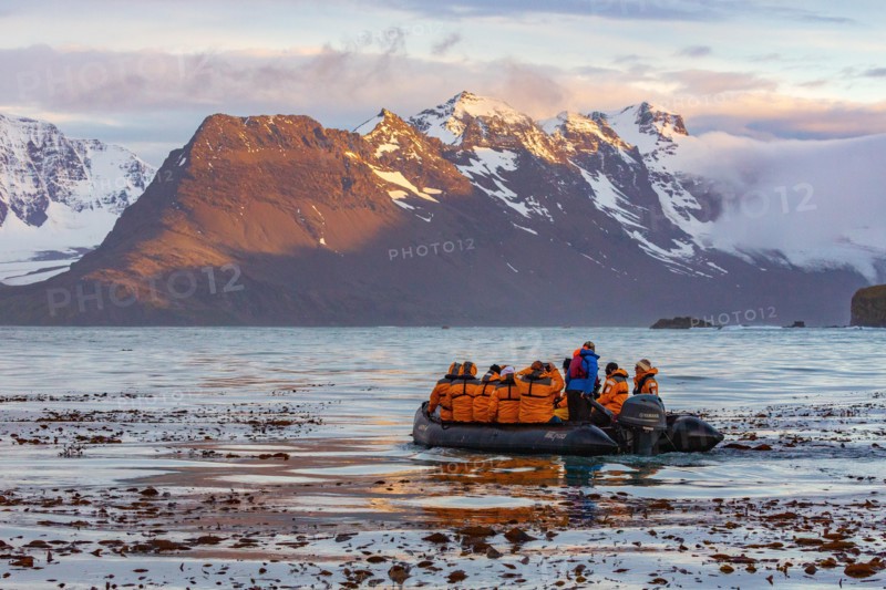 sunset on the snow capped mountains of the bay of isles in south Georgia in the foreground is a zodiac boat from an Antarctic cruise ship