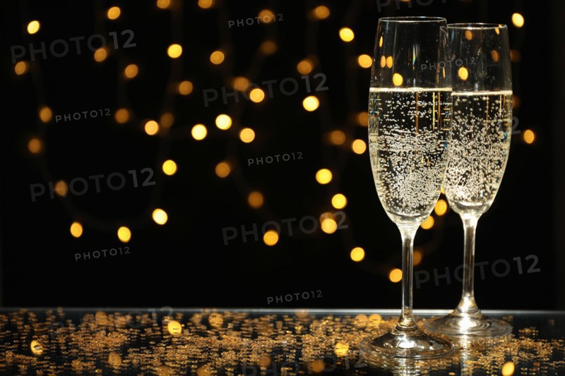 Champagne glasses against blurred lights background, space for text