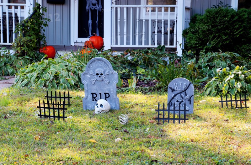 Front yard of private house decorated by fake skull, bones hands, tombstones and grates, pumpkins on the porch for a old american trick-or-treat Hallo