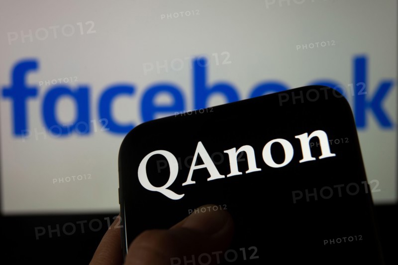 QAnon vs FACEBOOK. QAnon organisation logo seen on the smartphone which is placed on Facebook logos. Concept for ban of QAnon on social media.