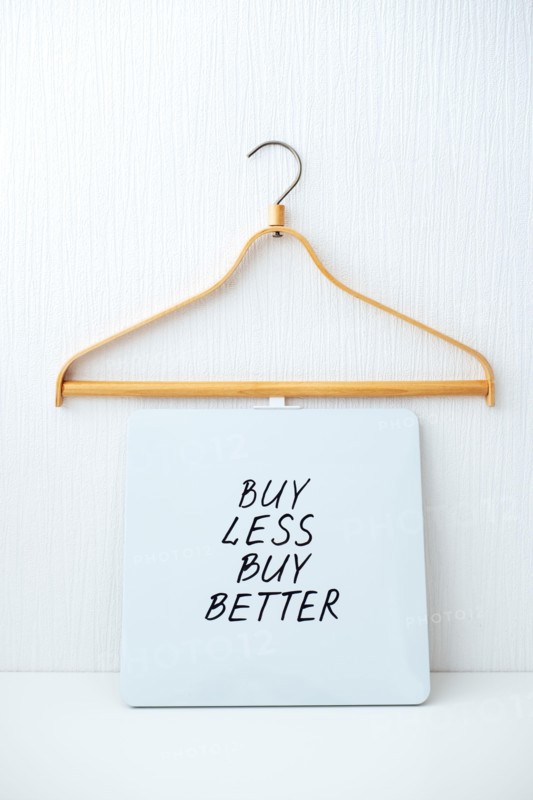 Sustainable consumption and production. Circular economy, Sustainable fashion concept with wooden clothes hangers and text Buy less, buy better