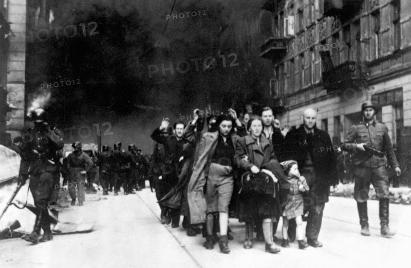 In January 1943 the nazis arrived to round up the Jews of the Warsaw Ghetto  The Jews, resolved to fight it out, took on the SS with homemade and primitive weapons. The defenders were executed or deported and the Ghetto area was systematically demolished. This event is known as The Ghetto Uprising. This image shows a column of captured women leaving the burning city.  This image is from the German photographic record of the event, known as the Stroop report.