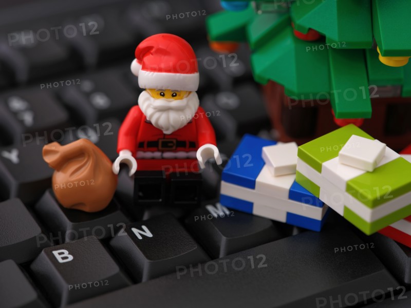 Tambov, Russian Federation - October 31, 2023 A Lego Santa Claus minifigure sitting on a computer keyboard next to Christmas tree and some presents. C