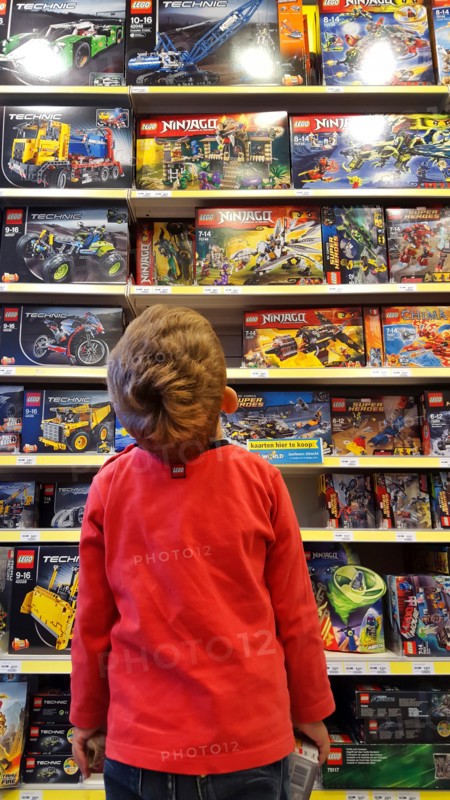 little boy admiring a plaything-shelf with LEGO packings