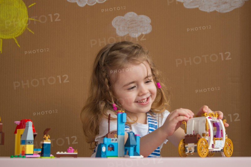 Cute funny preschooler little girl playing with construction toy blocks in kindergarten room. background painted by the sun and clouds