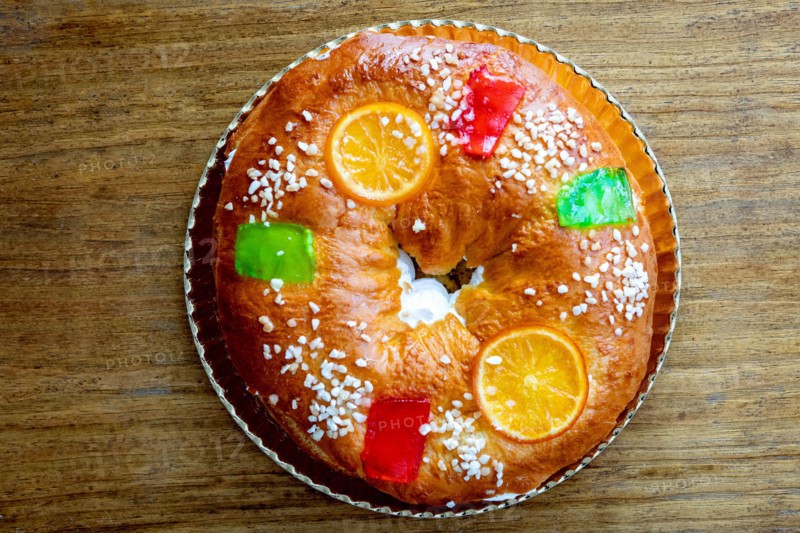 Christmas round fruit cake decorated with fir tree branch, glazed fruits and nuts on a wooden background.