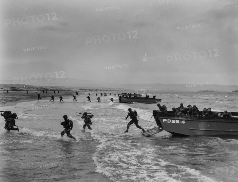 Invaders Hit the Shore in Invasion Maneuvers - American troops, carrying rifles and light fighting equipment, spring through the surf from Coast Guard-manned landing craft in final amphibious maneuvers somewhere on the North African coast. Invaders and Coast Guard invasion craft, such as these, hit the beaches of French Normandy before dawn D-Day