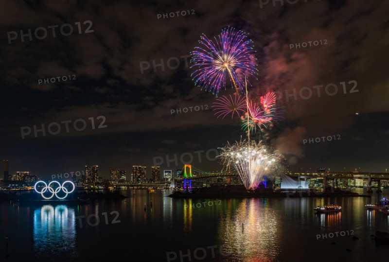 A picture of the fireworks commemorating the opening of the Olympic Rings in the Tokyo Bay, featuring the Rainbow Bridge, at night (Tokyo).