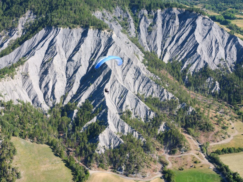 AIR-TO-AIR VIEW. Paraglider soaring above a landscape of eroded ravines. Barcelonnette, Alpes-de-Haute-Provence, France.