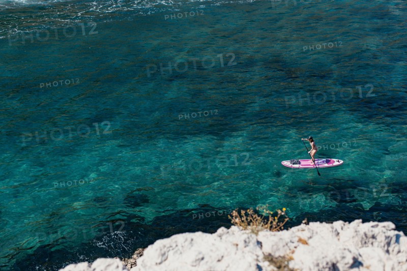 A woman is enjoying a session on a stand up paddle SUP on crystal clear waters in the South of France in Summer
