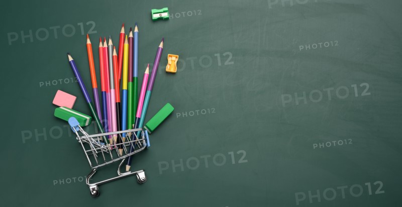 Miniature shopping cart full of school office supplies on a green chalk board. Preparing for school, buying pens and notebooks