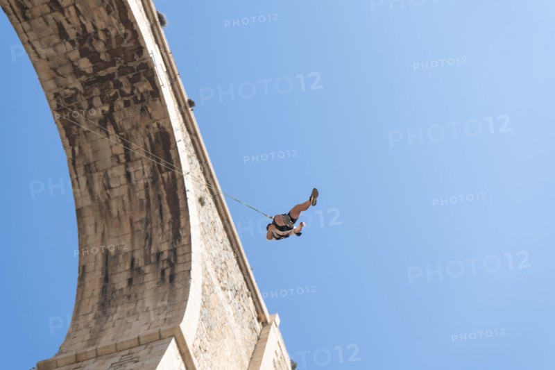 Low angle view of a person swinging after bungee jumping from a historic stone bridge. Adventure sports concept. Space for text