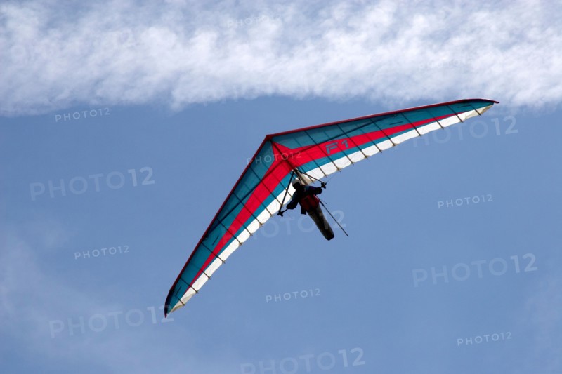 Hang gliding pilot flying blue red and white hang glider against sky in mountains of French Alps Haute Savoie France