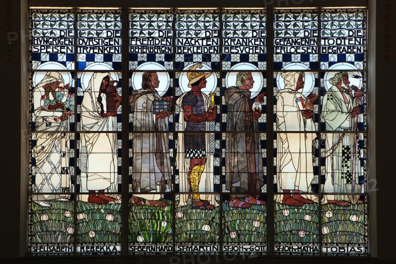 Stained glass window 'The Seven Corporal Works of Mercy' designed by Austrian artist Koloman Moser (1907) in the Steinhof Church (Kirche am Steinhof) in Vienna, Austria. Saints and Old Testaments characters are depicted in the stained glass window from left to right: Saint Elizabeth of Hungary, Rebecca, Saint Bernard, Saint Martin of Tours, Saint John of God, Saint John of Matha and Tobias.