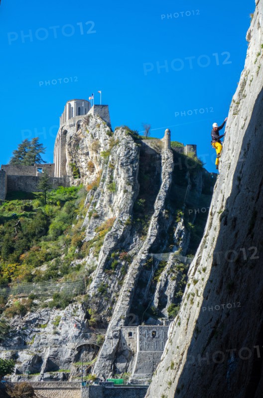 Rock climber in yellow climbing in canyon with castle beyond