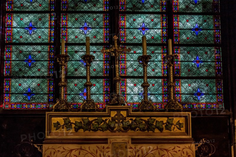 Alter candles in brass candler holders with a  stunning blue and green stained glass window behind in Notre Dame Cathedral ,Paris