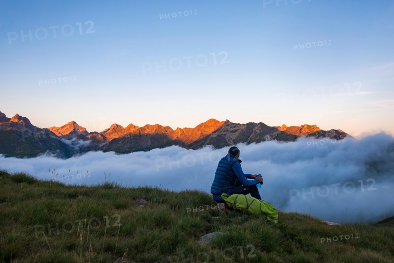 A hiker watches the sunset on the Pyrenees and a cloud inversion near Refuge Pombie along the GR10 trekking route, Pyrenees Atlantiques, France