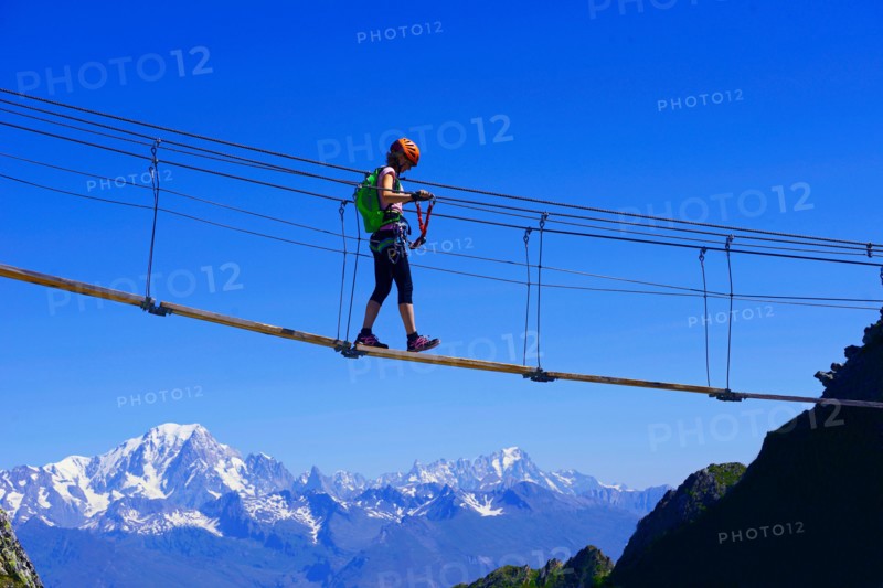woman crossing a simple suspension bridge, Via Ferrata of La Plagne, Mont Blanc in background, France, Savoie, Tarentaise