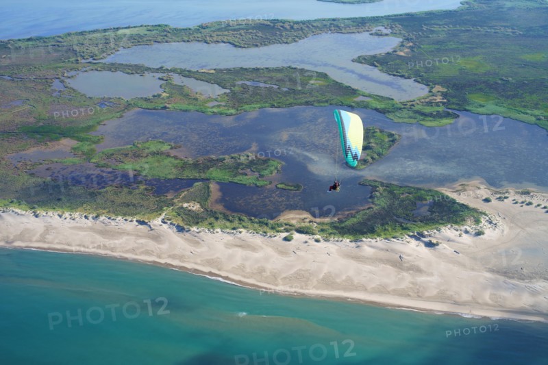 AERIAL VIEW. Paramotorist flying above a landscape of marshlands alongside the seacoast. Camargue marshes of the Rhone Delta, Arles, Provence, France.