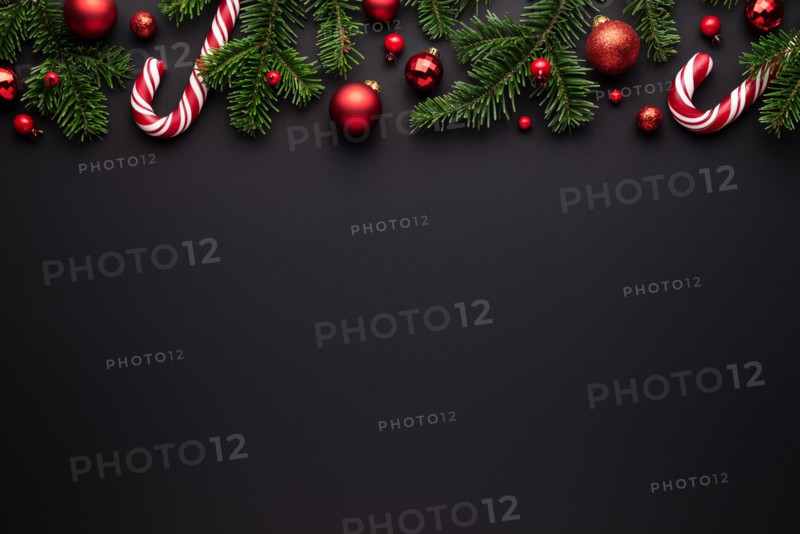 Black Christmas background. Decorative border of fir branches, red Christmas balls and Candy canes. Copy space for text