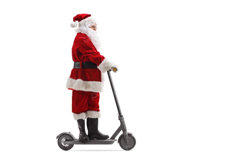 Full length portrait of Santa Claus riding an electric scooter isolated on white background