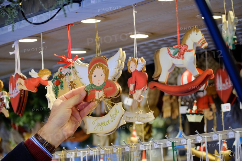 Man's hand grabbing cute christmas ornament with "Joyeux Noel" hanging on display from a stall, amongst other ornaments at the Strasbourg Christmas Ma