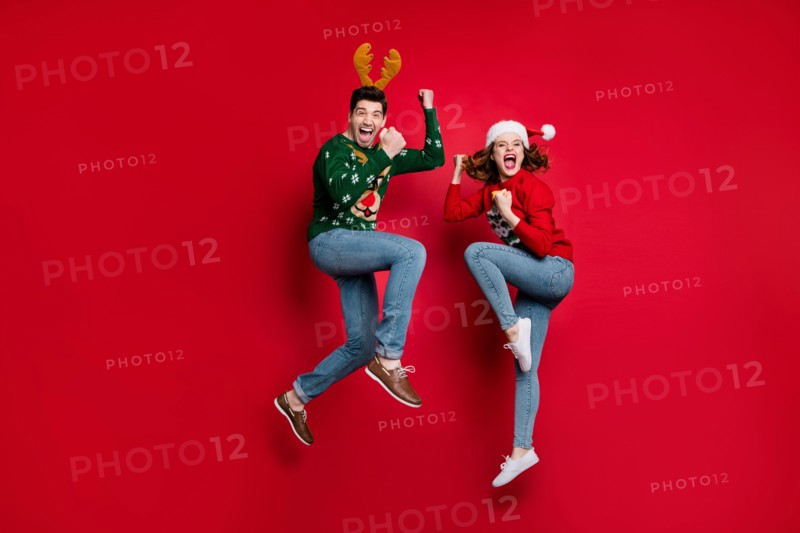Full body photo of amazed jumping couple excited by x-mas prices wear ugly ornament jumpers and headwear isolated red color background