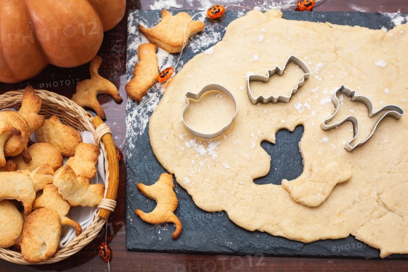 Making cookies for Halloween. Cut out cookies from dough in the form of pumpkin, cat, ghost and bat.