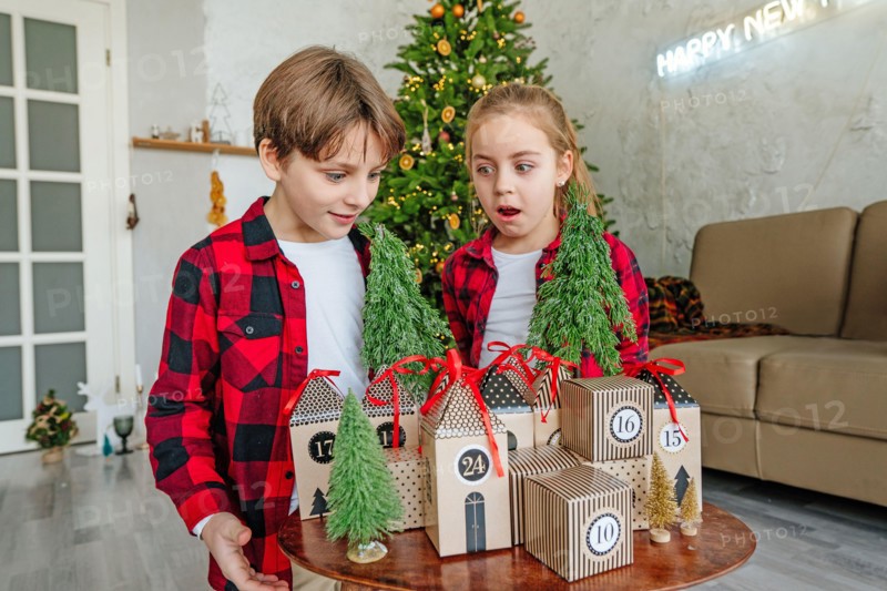 Children opening Christmas handmade advent calendar in a house shape to countdown the days until Christmas in the room.