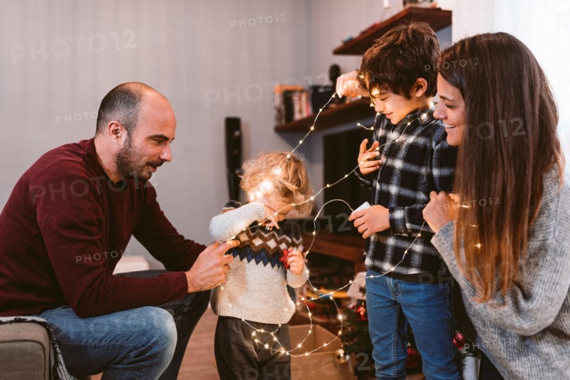 happy family christmas time at home. smiling mother and father with cute children decorating christmas lights together. family unit and christmas spir