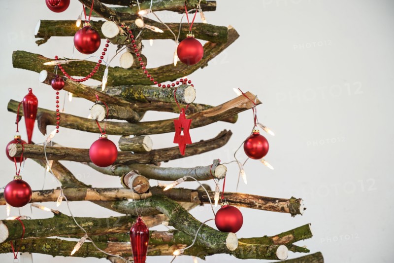 Homemade rustic Christmas tree made of raw wood branches, decorated with fairy lights and red balls, sustainable and environmentally friendly alternat