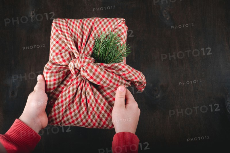 Children's hands holding gift wrapping in natural fabric in the style of Furoshiki. Sustainable gifts. Zero waste. Xmas eco holiday. High quality phot