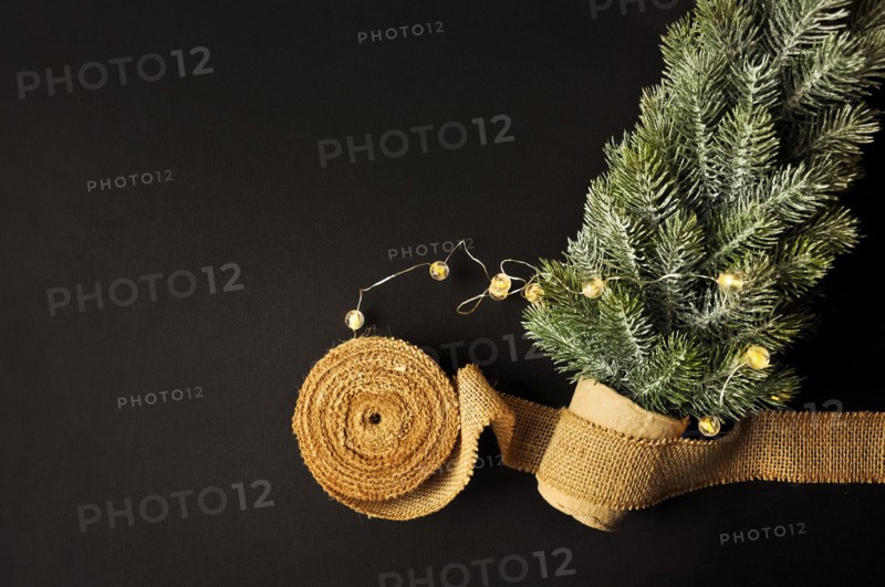 Preparation of decorations for winter celebrations. Artificial Christmas tree, natural jute fiber strip, dark background, cozy lighting