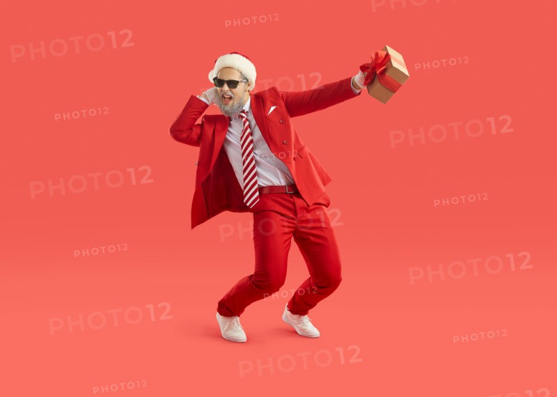 Cool energetic man in santa hat having fun and dancing with christmas gift in hand.