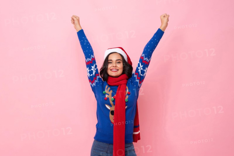 Festive portrait of joyful woman wearing Christmas sweater and hat raising hands up in pink color isolated background studio shot