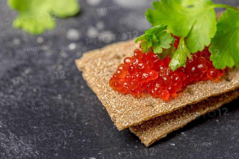 Grain crispbreads with red caviar and parsley at black background. Tasty sandwich, Christmas dish