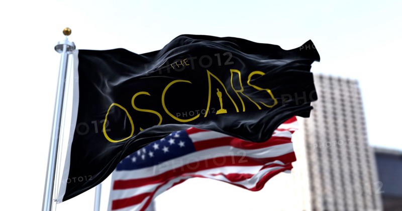 Hollywood, CA, USA, March 2022: the flag with the Academy Awards logo waving with the American flag blurred in the background. The Academy Award, aka