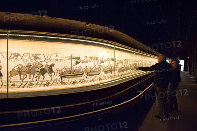 A couple of tourists admiring the Bayeux tapestry or La Tapisserie de la Reine Mathilde in it's current display case