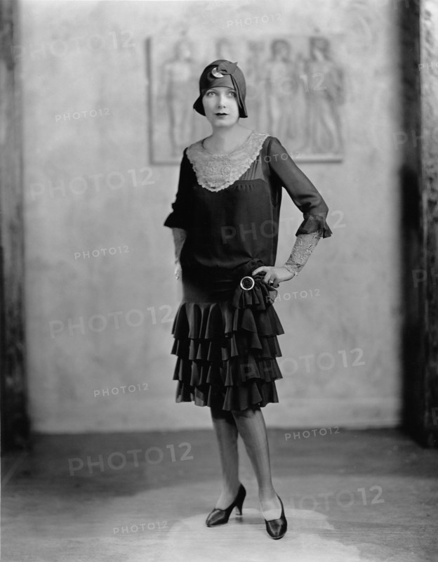 Young woman in a 'flapper' dress and cloche hat posing for portrait with hands on hips. Circa 1922