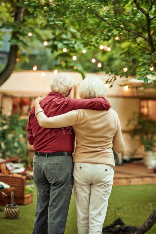 Back view of senior married couple looking at their campervan and hugging while standing outdoors. Travel concept