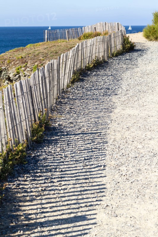 Typical french coast sea view with a pathway to the beach and wooden fence creating beautiful shadow.