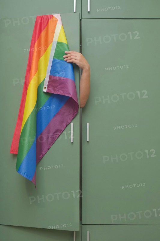 Hand holds to hide rainbow flag back inside closet. Fear of coming out concept. Internalized shame with homosexuality metaphor. LGBT guilt symbol.