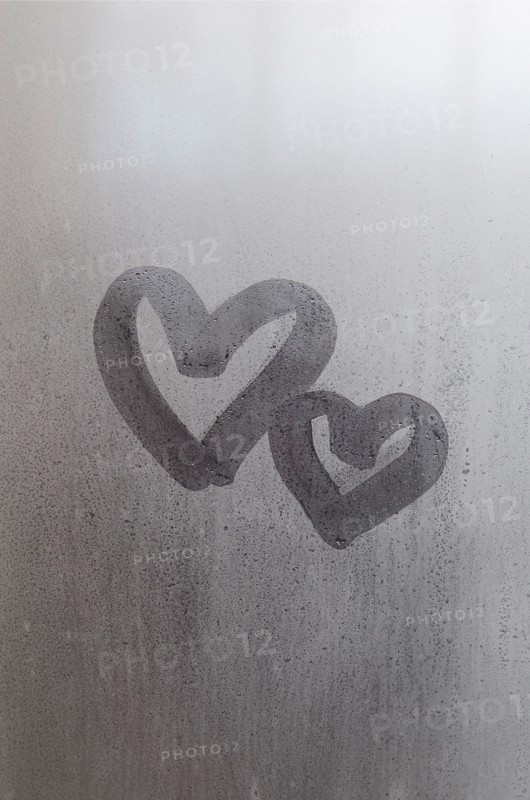 Couple of abstract blurred love heart symbol drawn by hand on the wet window glass with sunlight background. Template for Valentine Day postcards