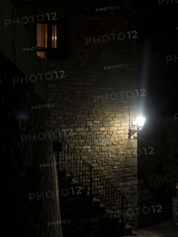 atmospheric night scene featuring a dimly lit stone building with a glowing window and street lamp