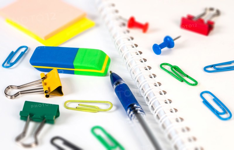 A variety of stationery items, like an eraser, paper clips, and a notebook, are neatly laid out on a clean workspace for school projects.