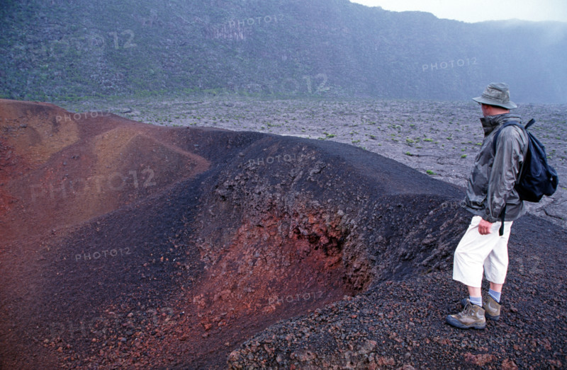 Tourist standing on the edge of Formica Leo crater, Piton de la Fournaise volcano, La Reunion Island, Indian Ocean