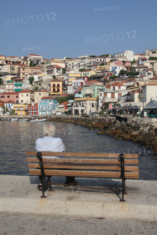 man sitting on bench in the port at parga, greece