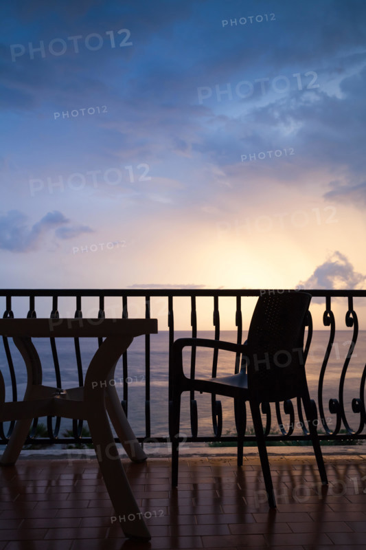 Armchair and table stand on a balcony. Seaside view over bright sunrise sky